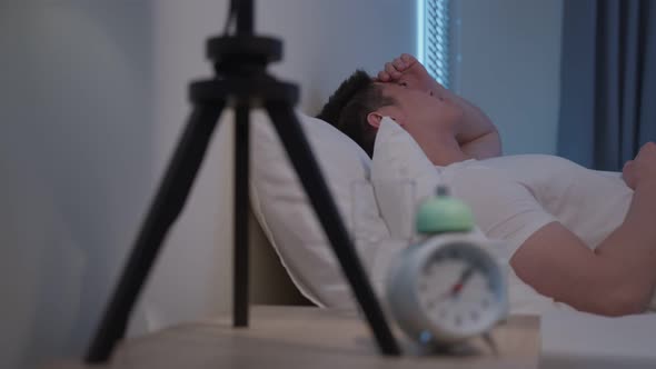 Asian sickness man in pajamas feel sick while sit on bed in bedroom. alt