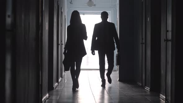 Silhouettes of Male and Female Office Workers Walking through Hallway 