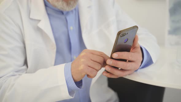 Cropped Male Doctors in Casual Wear Sit Using Smartphone at Home Thinking Indoors