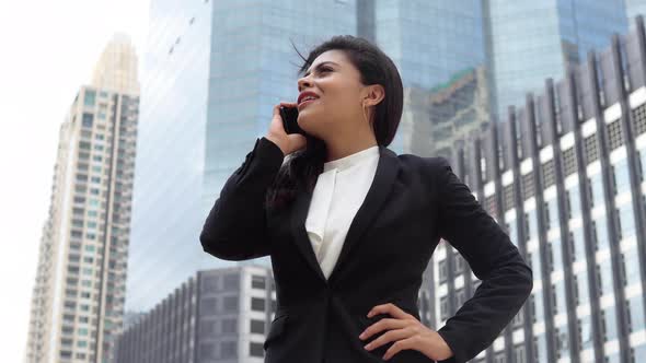 Young Indian businesswoman talking on cellphone standing in front of office buildings