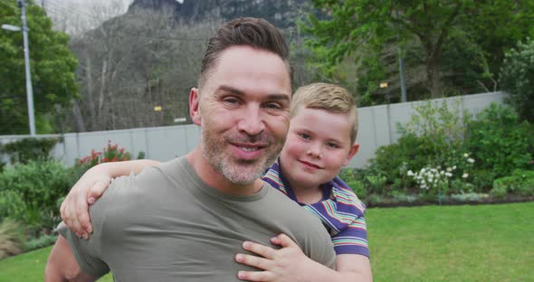 Portrait of caucasian father carrying his son on his back in the garden alt