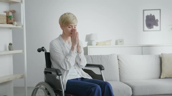 Mature Hopeless Woman in with Spinal Injury Praying to Gao Sitting in Wheelchair at Home Interior alt