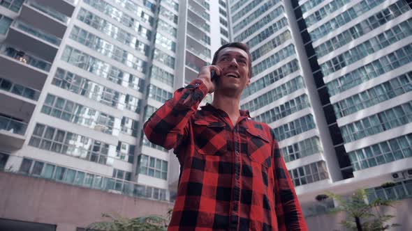Young Man With Smartphone Standing Outdoors In City Making A Phone Call alt