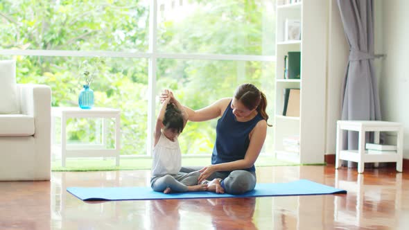 Young mother is teaching cute daughter basic yoga at home