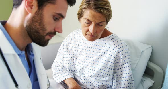 Male doctor discussing medical report with female patient on digital tablet alt