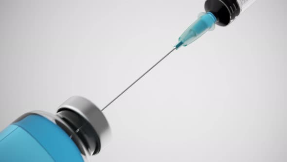 Long syringe needle drawing blue liquid from a container on a bright background. alt