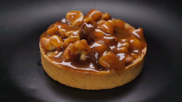 Tart With Nuts and Caramel Rotating on Black Plate