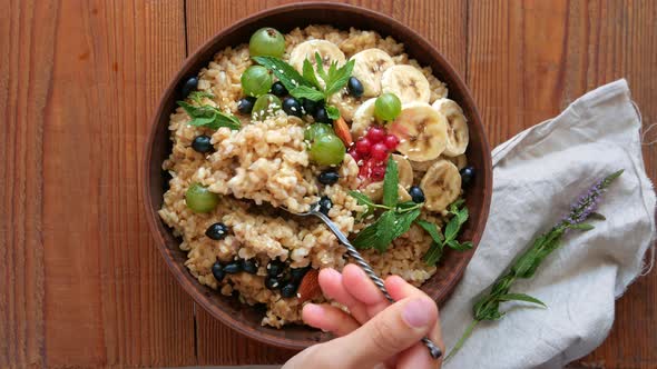 Wholegrain Oatmeal porridge with fresh berries, fruits nuts mint leaves sesame seeds in female hand
