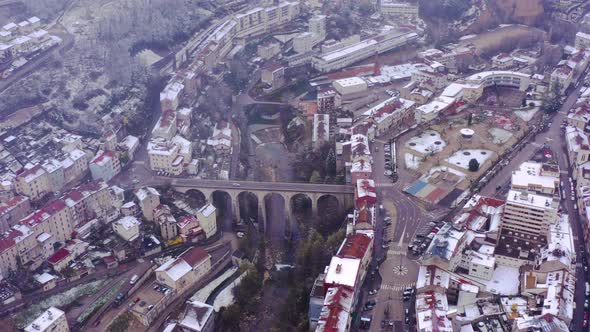Drone pull back from iconic bridge in heart of small town Saint-Claude. Snowy cityscape of France alt