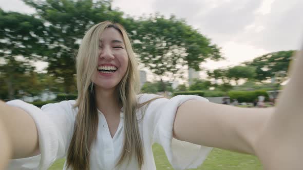 Happy beautiful young woman taking selfies using a smartphone at a public park.