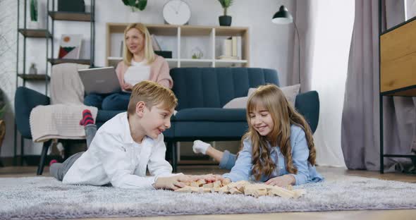 Brother and Sister Lying on the Floor and Talking Before Playing with Wooden Blocks alt