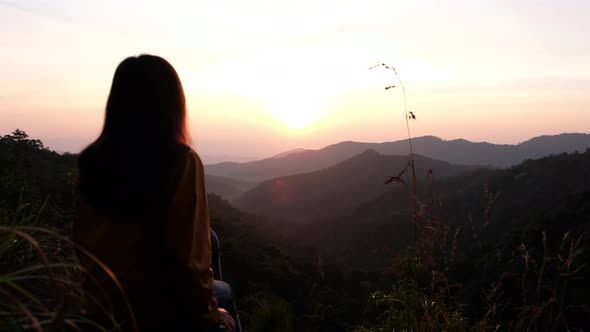 Blurred of a female traveler sitting on the mountain peak and watching sunrise in the morning