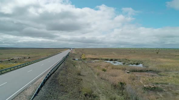 Aerial View of an Intercity Road Between Green Fields Against Blue Sky with Clouds alt