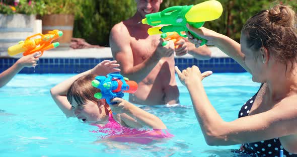 Happy family doing water gun battle in swimming pool alt