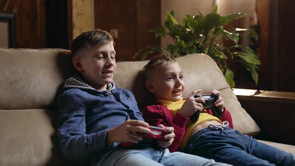 Schoolboys Sitting on the Soft Couch at Home and Playing Video Games with Joysticks alt