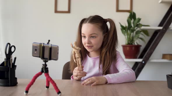 A Young Lady Bloggervlogger Talks to the Camera of the Phone Standing on the Tripod About Her Toy alt