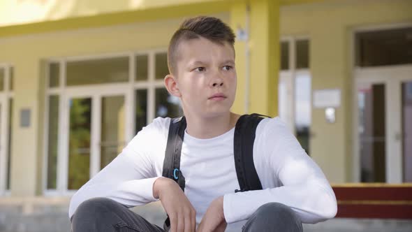 A Caucasian Teenage Boy Looks Around As He Sits in Front of School  Closeup