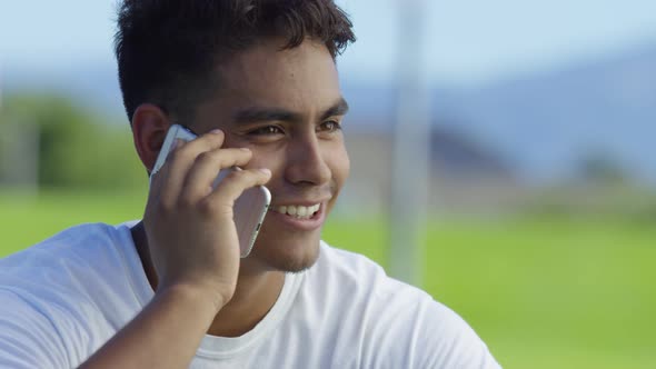 Teen basketball player talking on cell phone at outdoor court