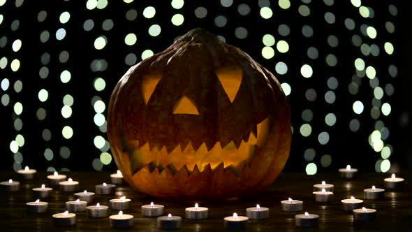 Halloween Pumpkin Lights Inside with Flame on a Black Bokeh Background with Lighted Candles alt