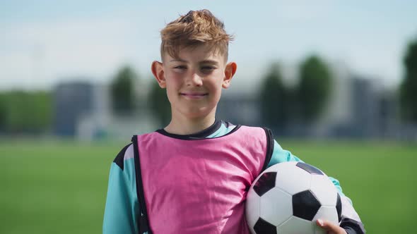 Portrait of a Football Player Boy, a Young Guy Stands Near a Football Field and Looks at the Camera alt