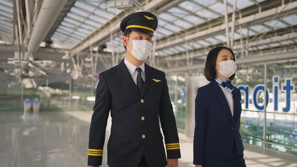 Airliner pilot and air hostess wear face mask walking in airport terminal to airplane during Covid19 alt