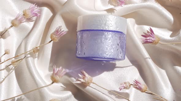 Blue glass cream jar mockup on smooth silk fabric sunlight flowers shadow water splashes Skincare 4K