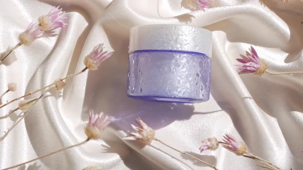 Blue glass cream jar mockup on smooth silk fabric sunlight flowers shadow water splashes Skincare 4K alt