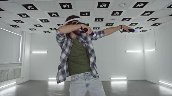 Young Man in Virtual Reality Glasses Dances in a Videogame in an Empty Playroom Full of White Neon
