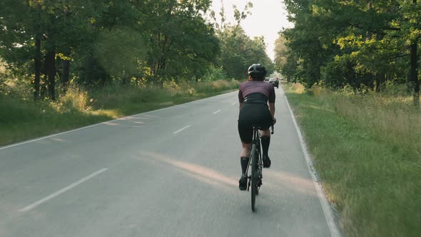 Woman cycling. Cyclist training on road bike at sunset. Cycling training at sunrise. alt