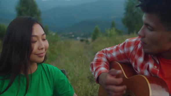 Relaxed Multiracial Couple Travelers Enjoying Leisure Playing Music on Mountain Hill alt