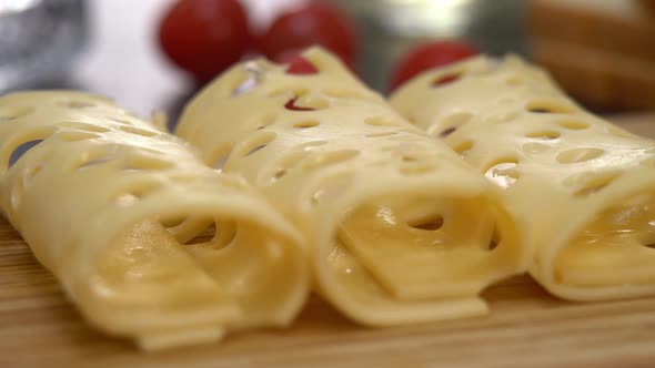 Slices Rolled Cheese with Holes on Background of Tomato and Bread alt