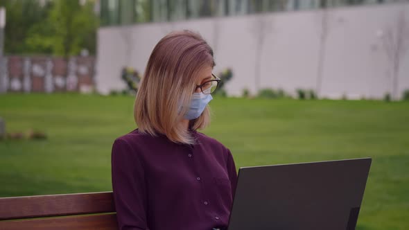 Woman portrait works on laptop outdoor sitting on park bench alt