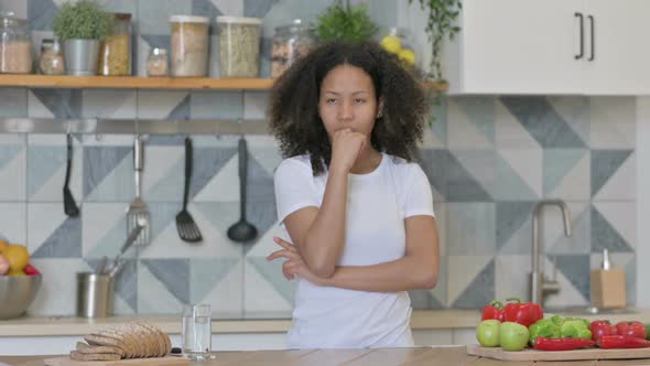 Young African Woman Thinking While Standing in Kitchen alt