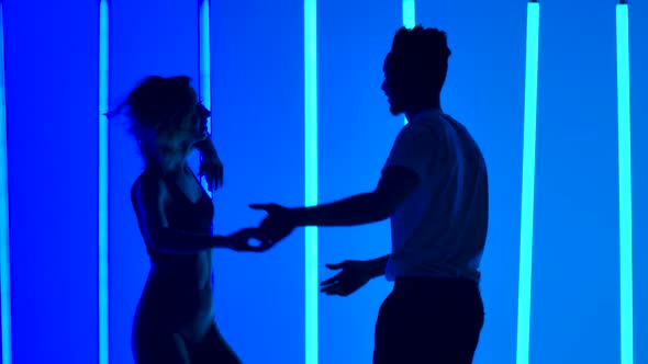 Dancers Practice a Series of Spins Against a Backdrop of Bright Blue Neon Lights in a Dark Studio alt