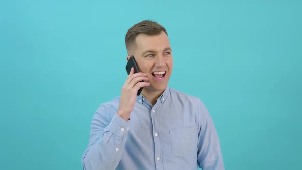 Caucasian Middleaged Man in a Blue Shirt Raises a Smartphone to His Ear and Talks alt