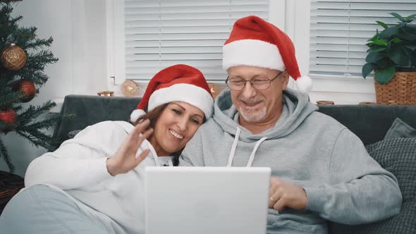 A Happy Middleaged Couple with Santa Hats Congratulate Their Relatives and Friends Via Video Link on