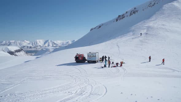Group of hikers transported by tracked vehicle near snowy mountain slope to start hiking alt