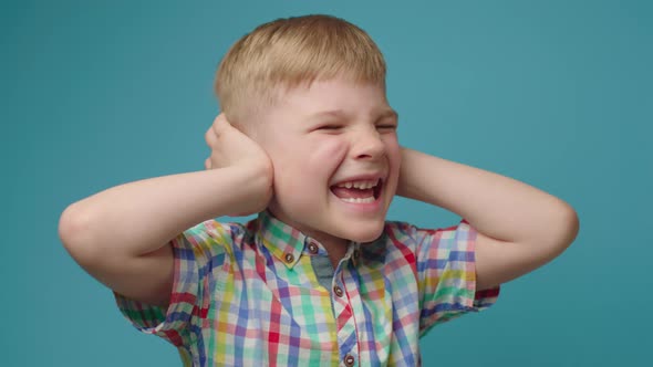 Smiling Boy Closing Ears with Hands and Crying 'NO I Don't Hear You' Standing on Blue Background alt