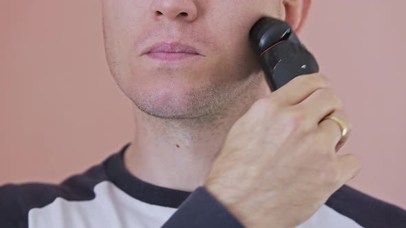 Young Man is Shaving His Beard with an Electric Shaver