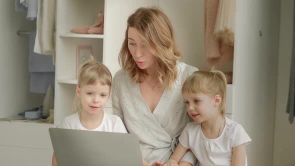 Mom with Twin Daughters Sitting at a Laptop and Looking Out the Window