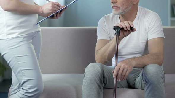 Nurse writing down medical records, talking to old male patient at hospital alt