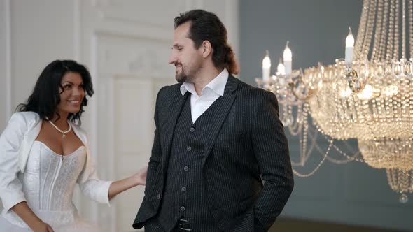 a Bride with Long Hair Comes Out From Behind the Groom and Hugs Him Against the Background of a alt