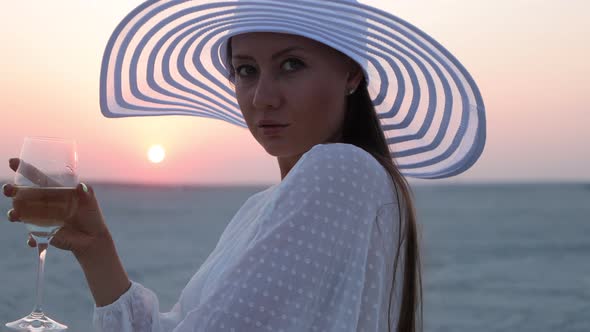 Elegant Woman with Glass of Wine Resting on Beach at Sunset