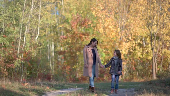 Happy mom walks with her daughter in the autumn park.