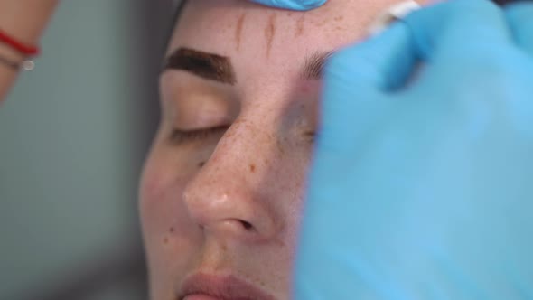 to a Young Beautiful Woman Hands in Gloves Remove Paint From a Painted Eyebrow with a Cotton Pad alt