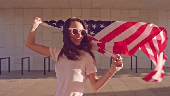 Young Cheerful Caucasian Woman in Sunglasses with Smile Holding Waving USA Flag alt