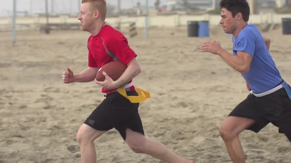 A group of guys playing flag football on the beach. alt