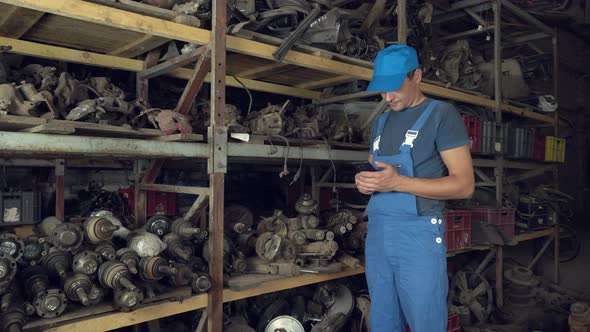 employee of auto disassembly, completes or checks car parts from tablet computer alt
