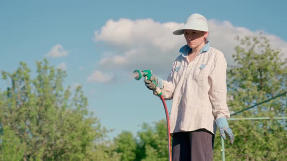 Woman Holding a Water Hose and Watering Beds or Plants in the Backyard alt