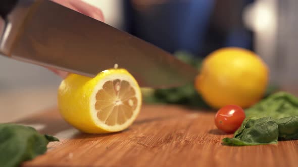 Woman's Hands Cutting Fresh Lemon on Wooden Cutting Board Using Kitchen Knife